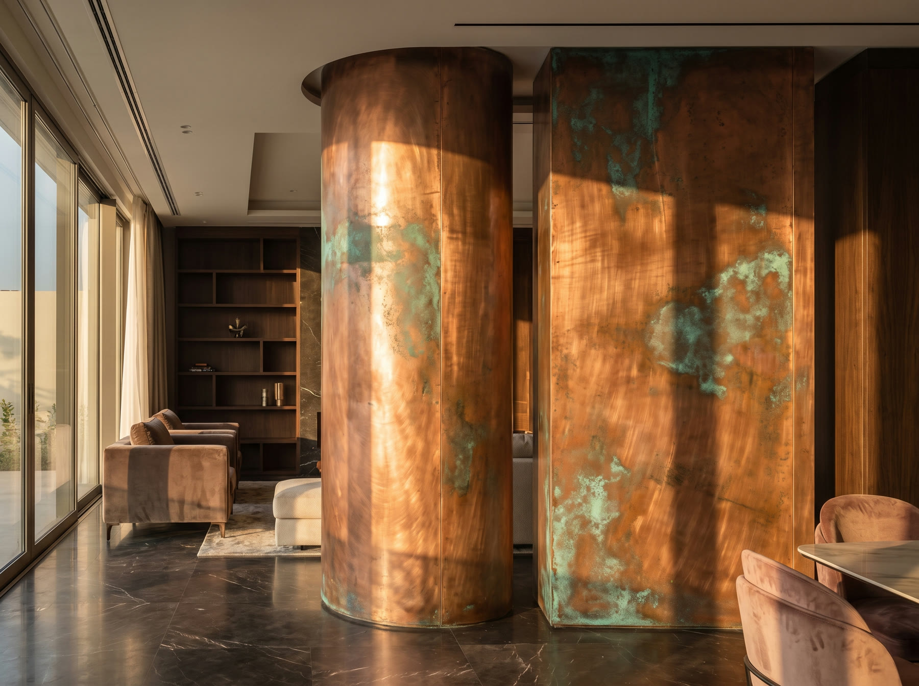 Two round wall columns clad in copper with soft green patina patches, lit by low evening sun in a living room