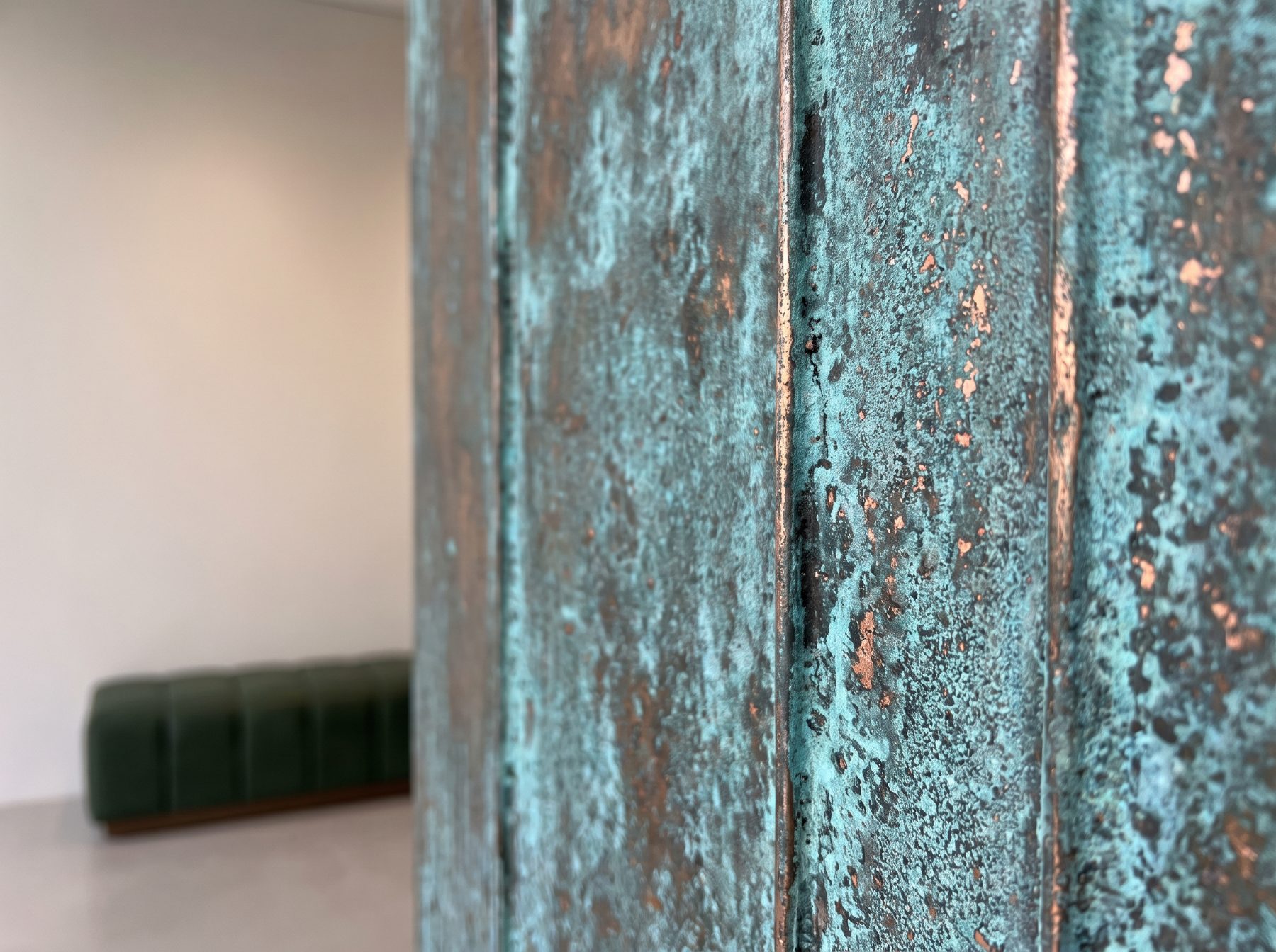 Close-up of a fluted wall column with blue-green verdigris and bare copper showing through, in a bright interior