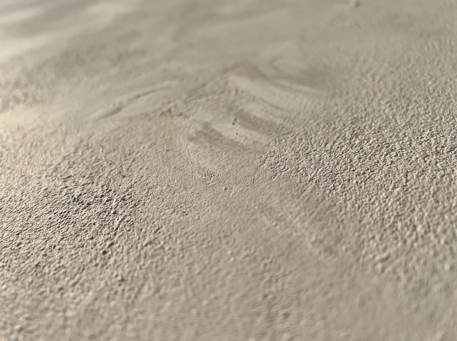 Close-up of a sand and stone-effect textured paint, showing the mineral grain holding light and shadow